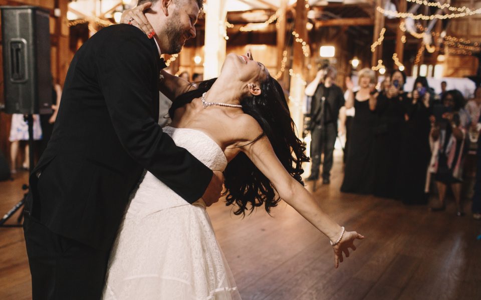 Groom bends brunette bride over while dancing in the wooden hall