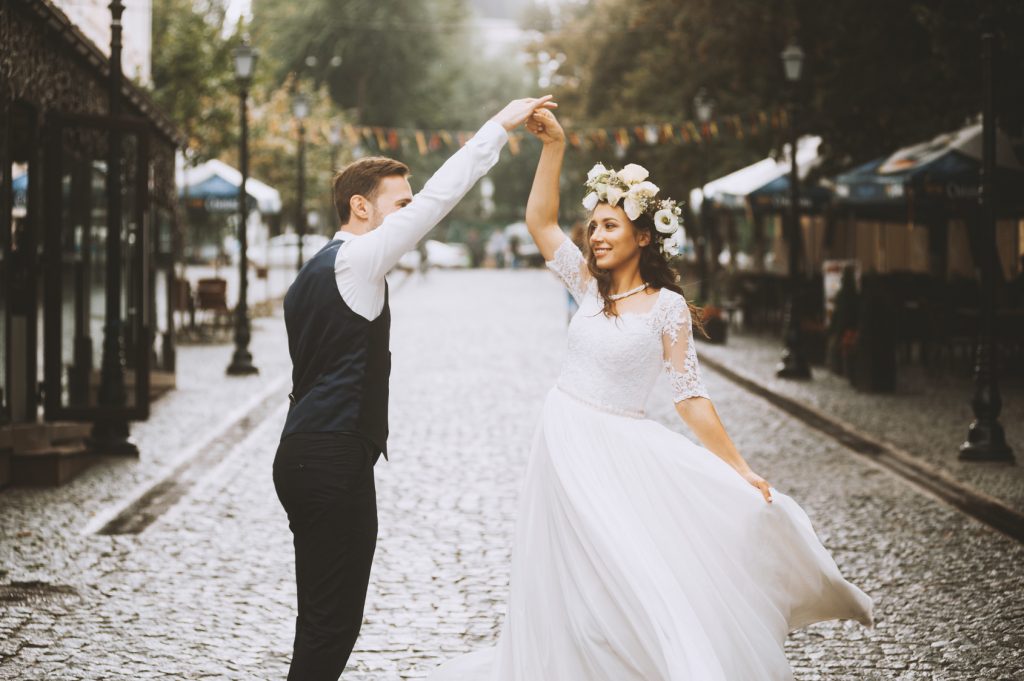 Beautiful newlywed couple is having fun while dancing in the sunny old town street